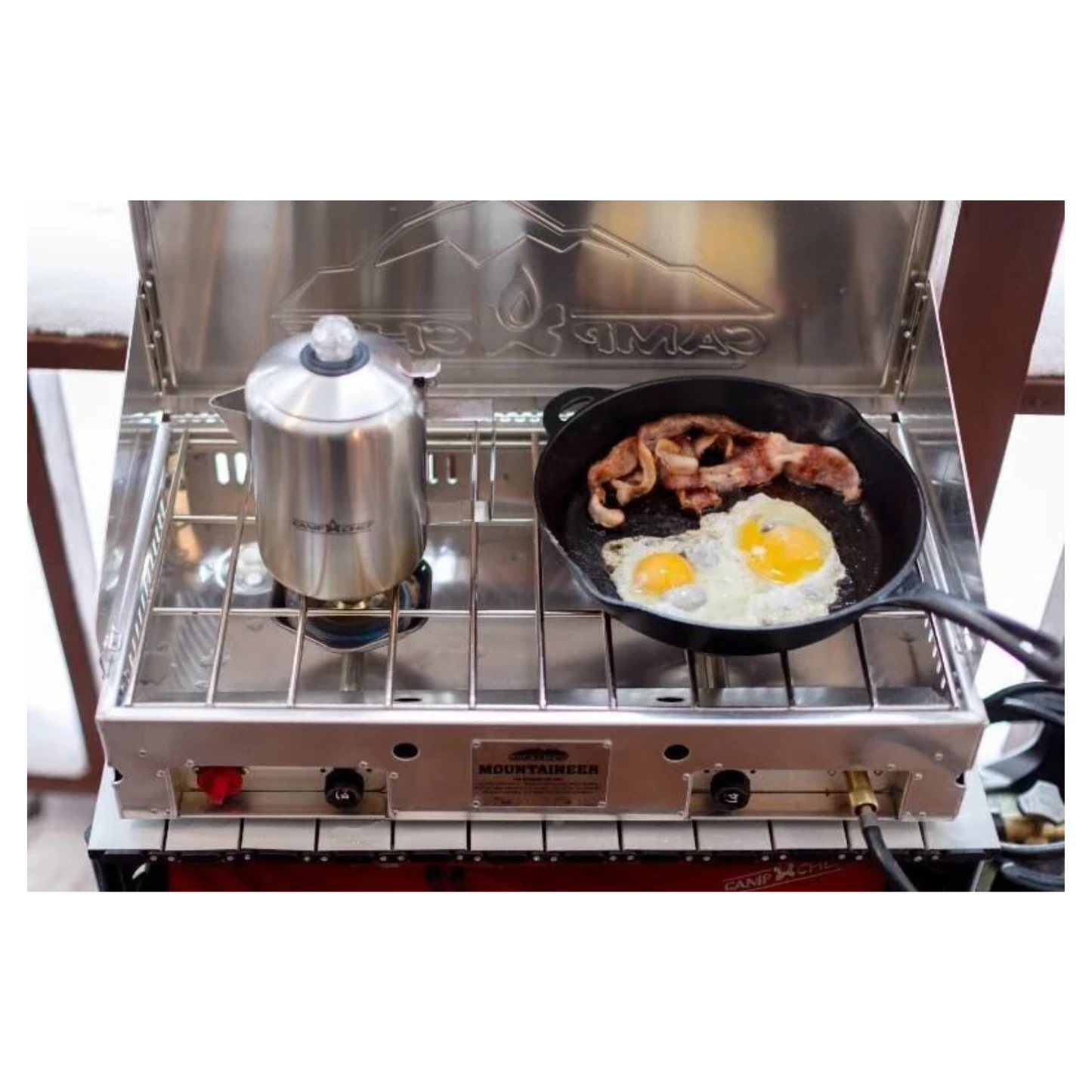 Portable stove with a pan of eggs and bacon on a white background
