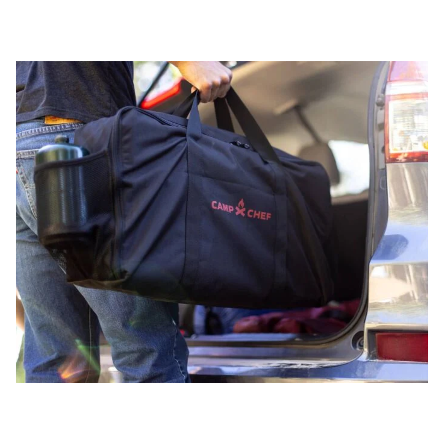 Black and red Camp chef bag for compact cooking system being put into the back of a SUV.