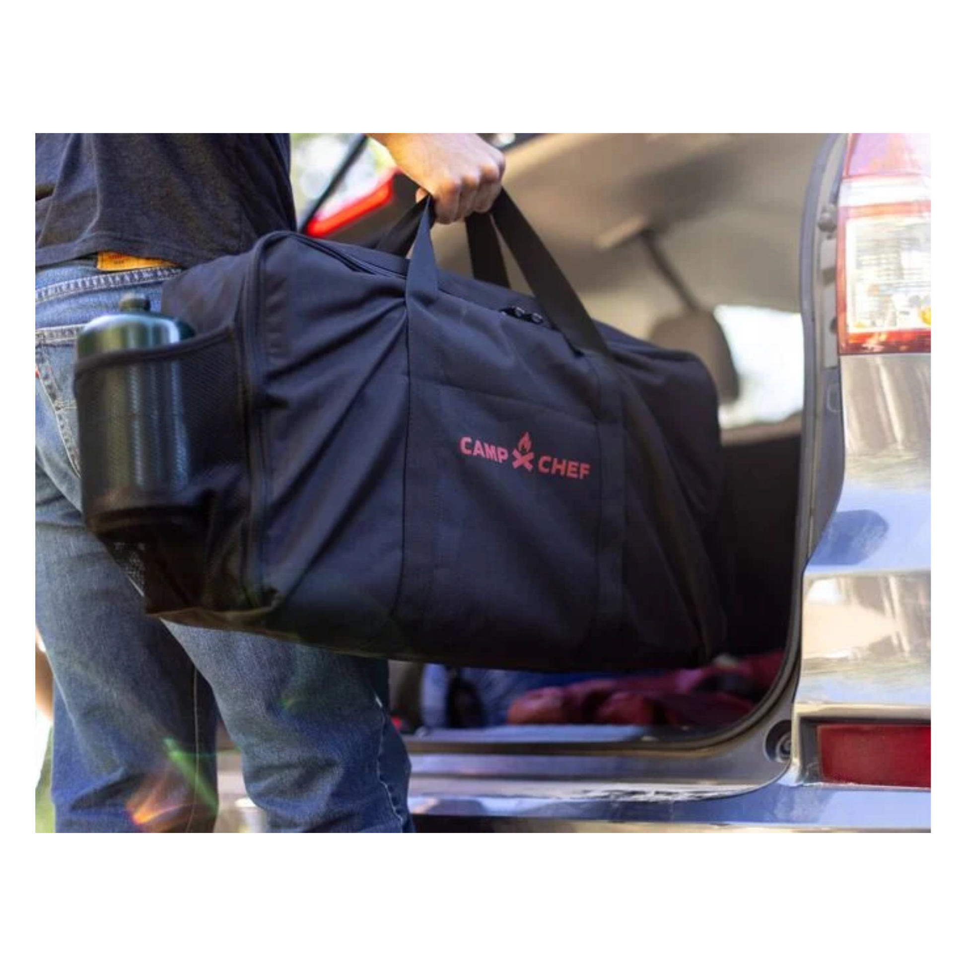 Black and red Camp chef bag for compact cooking system being put into the back of a SUV.