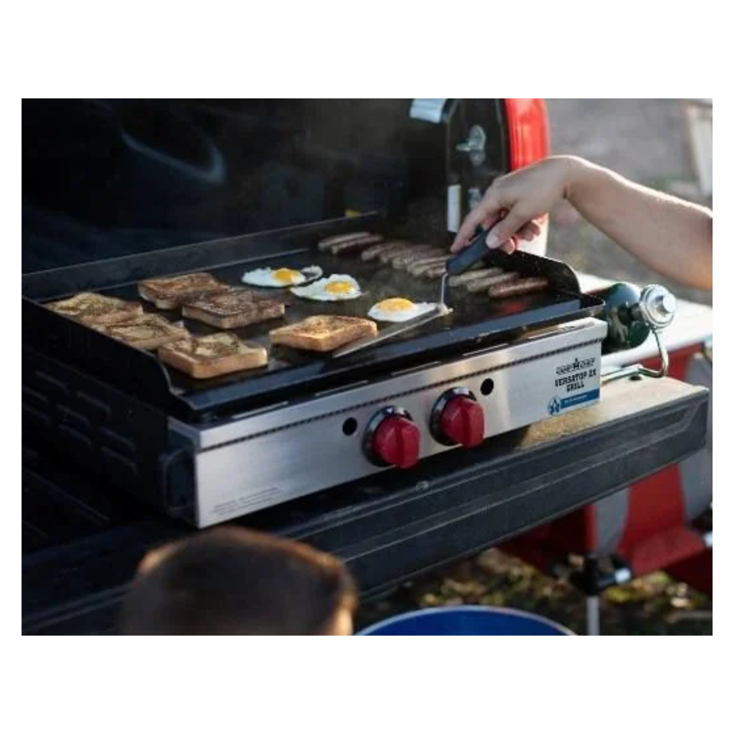 Person cooking on a portable grill with food items being prepared.